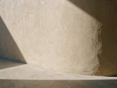 Close-up of a curved plaster wall meeting a concrete floor, soft natural daylight casting long architectural shadows, warm editorial photography, 35mm film texture.