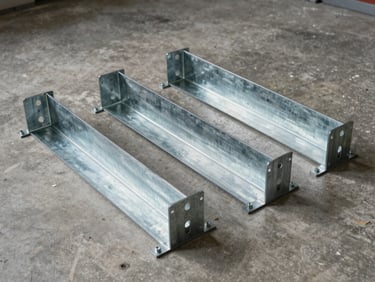 Studio strobe shot of modular steel enclosure sections and racking brackets laid out on a concrete floor, showing bolt patterns and galvanized finish under even lighting
