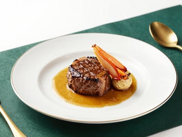 Premium plated corporate dinner, gourmet beef tenderloin with golden reduction, elegant cream porcelain plate, deep emerald table setting.