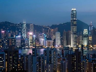 Atmospheric high-contrast wide shot of dense Hong Kong high-rises at dusk, illuminated by glowing neon signs, cool blue tone