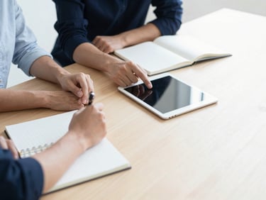 Two people collaborating over a clean wooden table with notebooks and a tablet, natural light, minimalist style