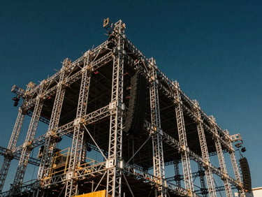 Low-angle shot of a massive aluminum stage truss structure under construction, metallic reflections, dramatic sky