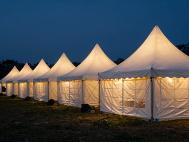 A row of clean white sarnavil tents illuminated from inside at dusk, professional outdoor exhibition setup