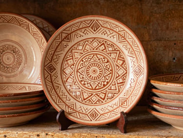 Close-up of hand-painted ceramic plates with intricate geometric Armenian stone carving motifs, stacked on a rustic wooden shelf