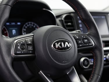 Close-up of a KIA vehicle instrument panel and steering wheel under clean studio lighting, sharp focus on controls and badge, no people