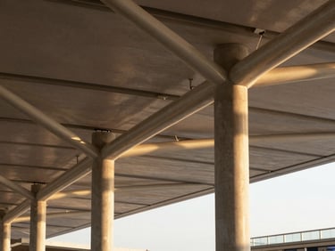 Close-up architectural detail of an airport terminal structural canopy, steel lattice and concrete columns, golden-hour light casting long structural shadows, no people visible