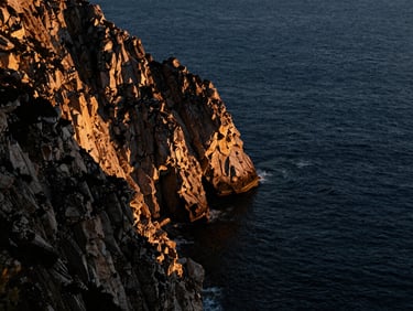 Dramatic coastal cliff overlooking deep blue ocean water, golden hour light, high contrast, 35mm