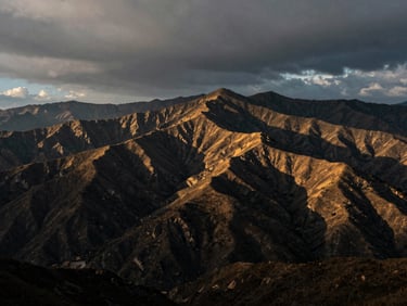 Cinematic wide panorama of rolling mountain ridges under a moody overcast sky, dramatic high-contrast lighting, 35mm