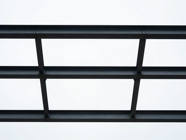 Looking up at a perfectly aligned grid of steel beams against a pure white sky, high-contrast architectural detail.