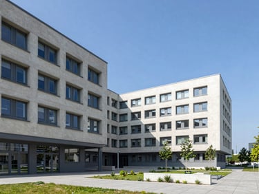 Wide environmental shot of a modern German university hospital campus, clean concrete architecture, blue sky, professional clinical setting.