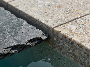 Extreme close-up of natural slate and gresite tile junction at a pool overflow edge, water bead on stone surface under flat north-facing daylight, material texture precise and documentary, no people