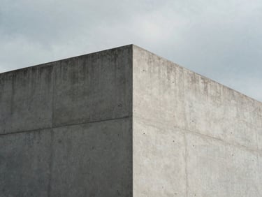 Minimalist architectural corner of a concrete building under cool overcast daylight, sharp geometric shadows, desaturated cool tones, 35mm photography.