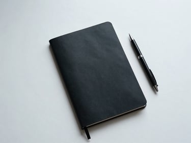 Overhead minimal view of a clean desk with an unmarked black notebook and a high-quality pen, cool diffused daylight.