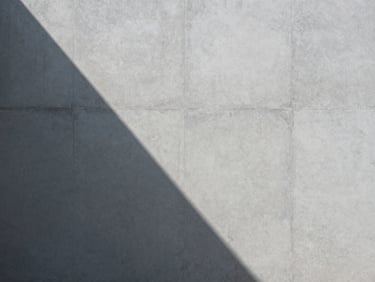 Abstract geometric pattern of light and shadow on a light grey concrete wall, sharp contrast, minimalist composition.