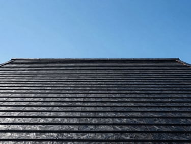 Wide architectural shot of a residential roofing project under clear skies, high contrast, crisp lighting.