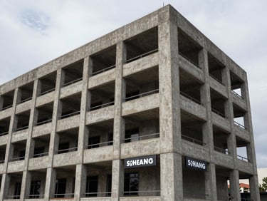Exterior facade of a finished four-story office building, concrete columns and recessed window frames under overcast north daylight, functional signage visible at ground level
