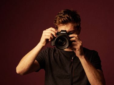 Low-key dramatic indoor scene of a young filmmaker adjusting a lighting gel, deep burgundy tones