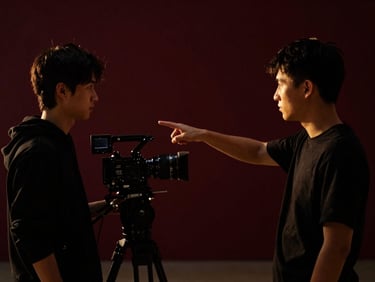A local film director pointing out a camera angle to a student on an indoor set, high-contrast dramatic low-key lighting