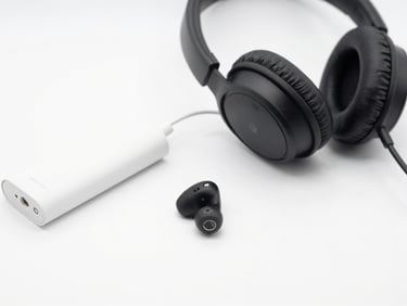 Um fone de ouvido sem fio e um carregador portátil dispostos de forma organizada sobre um fundo branco, com iluminação de estúdio brilhante e foco nítido nos detalhes.