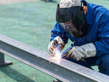 Professional welder in protective gear working on steel, bright sparks, clean blue and green tones