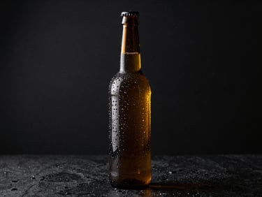 Botella de vidrio oscuro con gotas de condensación perfectas sobre fondo de piedra negra, iluminación de perfil dramática y reflejos dorados