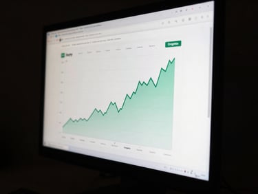 Close-up of a Shopify dashboard on a dark monitor showing a traffic spike line chart, organic sessions climbing sharply over six months, screen glow the sole light source, deep shadow surroundings