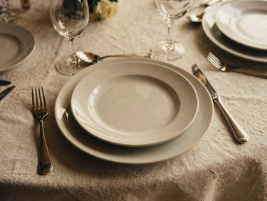 Styled overhead shot of a luxurious table setting with layered linens, unique plates, and elegant cutlery, warm light, rich tactile textures, 35mm film aesthetic.