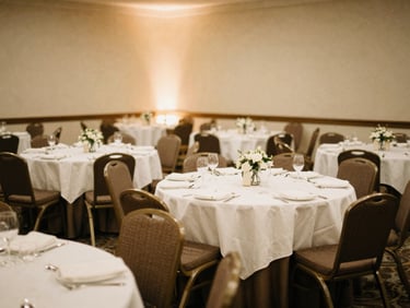 Wide shot of an empty reception hall, tables and chairs perfectly arranged, ready for guests, soft ambient lighting, warm editorial photography, 35mm film aesthetic.
