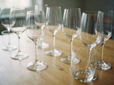 Arrangement of various elegant wine glasses and water goblets on a wooden table, reflections, soft natural light, shallow depth of field, 35mm film aesthetic.