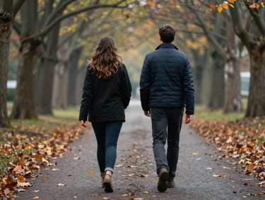Two people walking side by side on a tree-lined path in soft overcast light, seen from slightly behind, autumn leaves on the ground, intimate medium shot