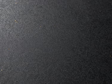 Macro shot of a matte black sintered stone surface, gold light catching the fine textured grain, architectural grade