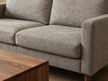 Close-up of a sculptural greige fabric sofa next to a low-profile walnut coffee table, warm diffused light