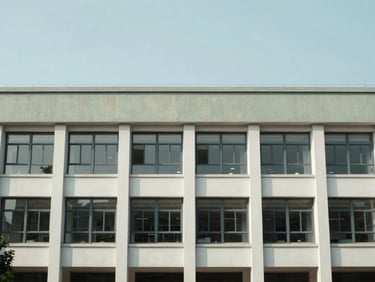 Architectural environmental shot of a modern institutional building facade, clear skies, soft natural daylight, muted cool tones.