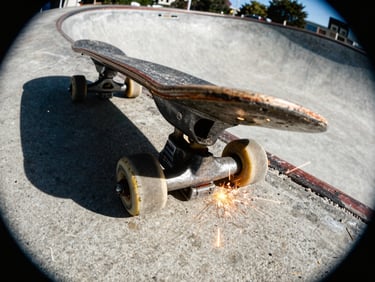 Close-up of worn skateboard trucks grinding a concrete pool coping, sparks flying, high-contrast sunlight.