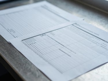 Macro shot of shipping documents and technical manifests on a steel desk, cool overcast daylight, sharp focus.