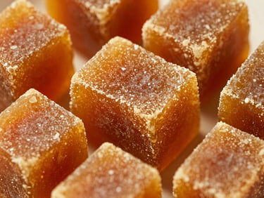 Macro shot of rich golden-amber jaggery blocks showing fine crystalline texture, warm natural sunlight