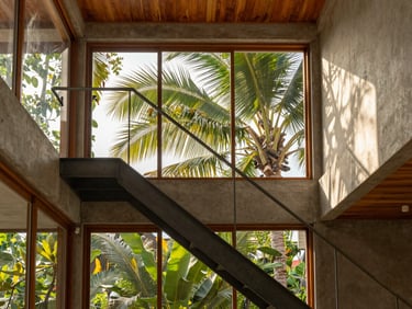 Architectural photography of a compact tropical home interior, high ceiling, natural light streaming through large windows, minimalist steel stairs