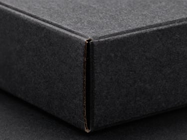 Macro studio shot of a rigid charcoal paperboard box with sharp 90-degree corners and clean paper seams under dramatic side light