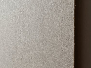 Close-up texture of raw, heavy-weight textured recycled paperboard in natural grey and bronze tones under soft raking light