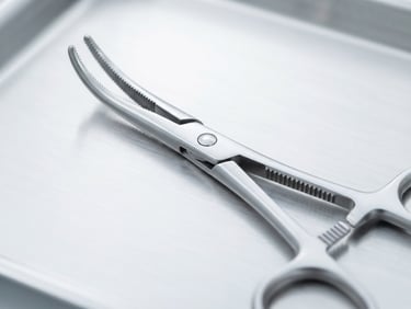 A macro close-up of sterile surgical forceps made of high-grade stainless steel, resting on a clean metallic tray under bright clinical white light, sharp focus, silver reflections.