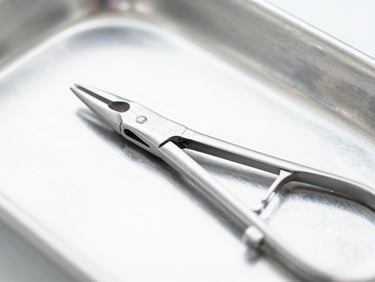 Macro close-up of surgical-grade stainless steel forceps resting on a sterile metal tray, bright clinical white light with soft silver reflections, sharp focus.