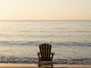 A wide panoramic view of a calm ocean at sunrise, gentle waves lapping the shore, a single, empty wooden Adirondack chair facing the water, soft amber light.
