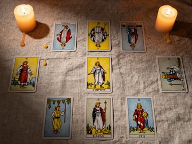 Close overhead view of a tarot card spread on aged linen cloth under candlelight, wax drips at the edges, deep shadow with warm amber glow catching card faces