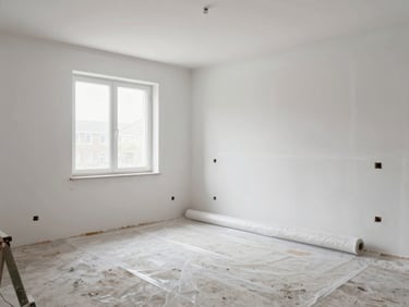 Wide shot of a renovated room with fresh white plaster walls, construction dust swept into corner piles, plastic sheeting being rolled up, diffused window light, no people