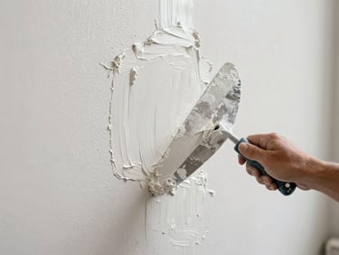Hands applying smooth white stucco to a wall with a wide trowel, fresh plaster texture visible up close, soft diffused daylight, no faces