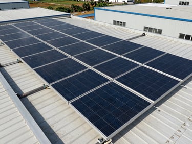 Close overhead view of a dense solar panel array installed on a flat industrial rooftop in natural Gulf daylight, connection conduits visible at panel edges, surrounding plant roofing in the background