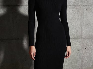 Studio fashion photography of a model in a sleek black ribbed knit dress, dramatic shadows, concrete backdrop, sharp focus