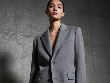 Low-angle fashion shot of a model wearing a structured gray blazer, industrial concrete background, high-contrast studio lighting