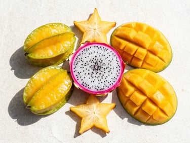Macro flat-lay of a custom tropical fruit platter with sliced starfruit, dragon fruit, and mango on a neutral white stone surface, bright direct sunlight, sharp shadows