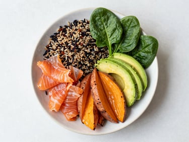 Overhead flat-lay of a vibrant salmon power bowl with wild rice, roasted sweet potatoes, fresh avocado, and bright green spinach on a clean ceramic plate, natural daylight